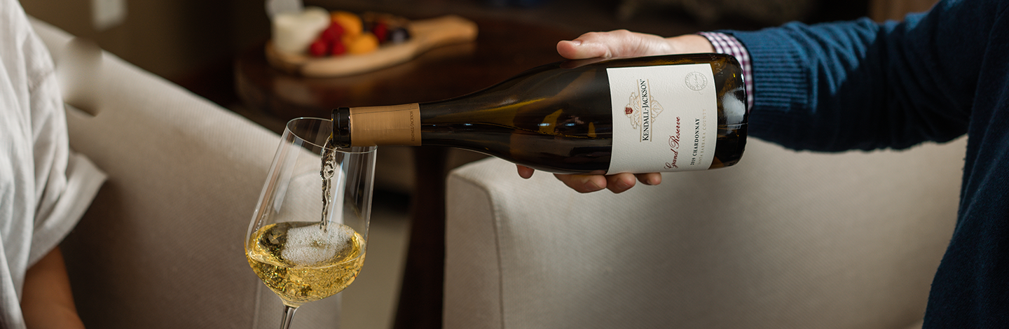 Close up of a person pouring Kendall-Jackson Grand Reserve Chardonnay into a glass.